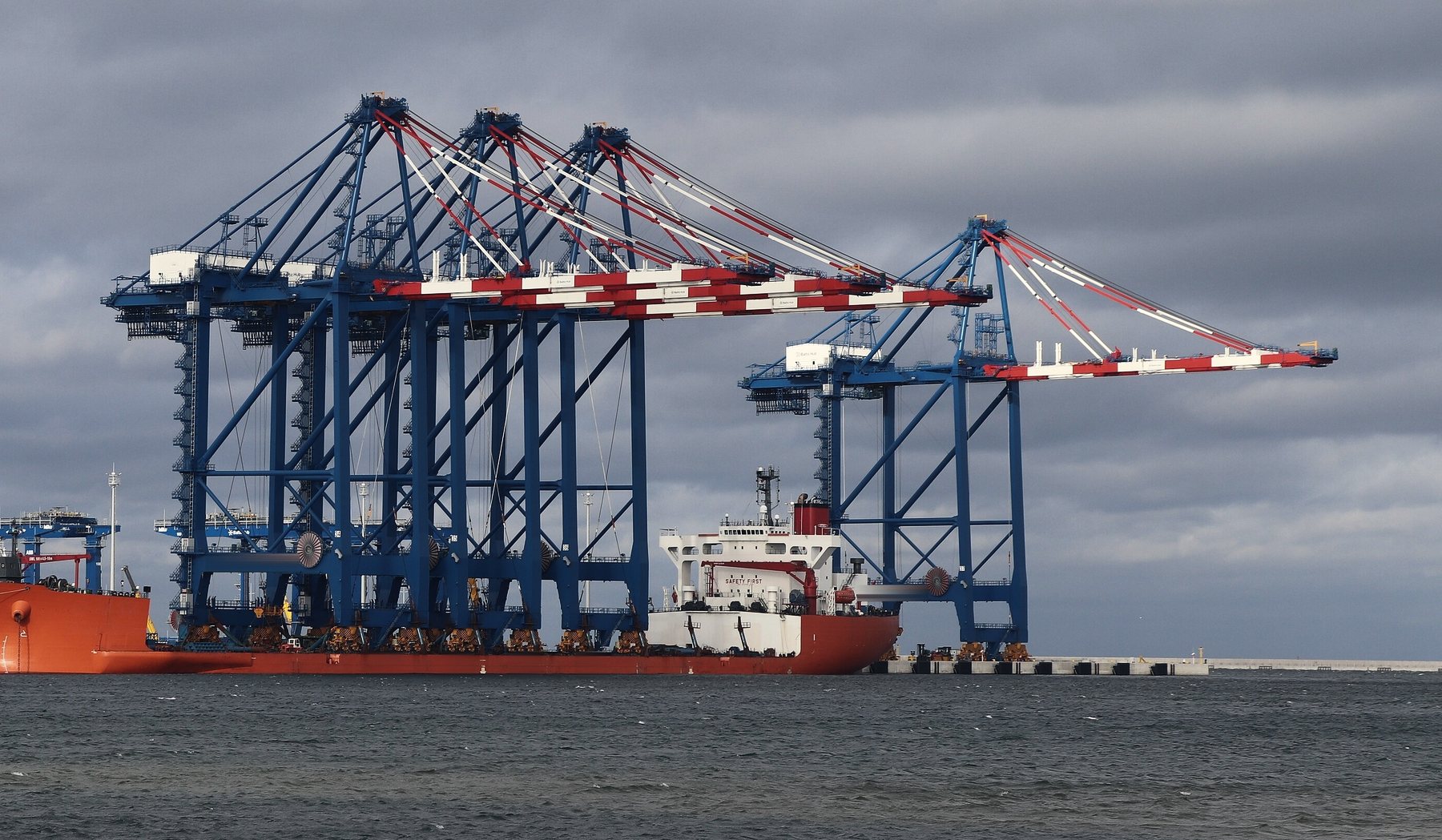 Four ship-to-shore container cranes arriving fully erected on the deck of a heavylift deck carrier, about to be rolled ashore at a container terminal